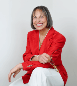 Judy M. Baker in red blazer holding her glasses
